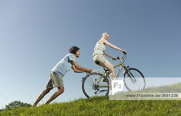 Eine Frau auf einem Fahrrad, Mann ihr bergauf schieben