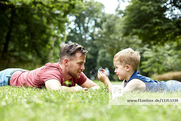 Vater und Sohn liegen mit Handy auf einer Wiese