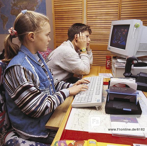 Side profile of girl playing game on computer with boy sitting beside her