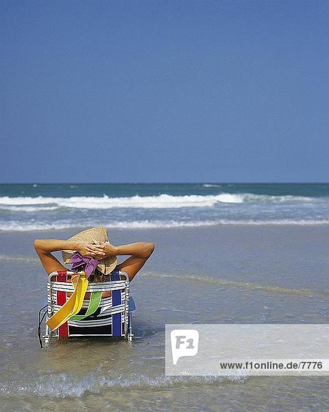 Rückansicht Frau sitzt auf Liegestuhl am Strand