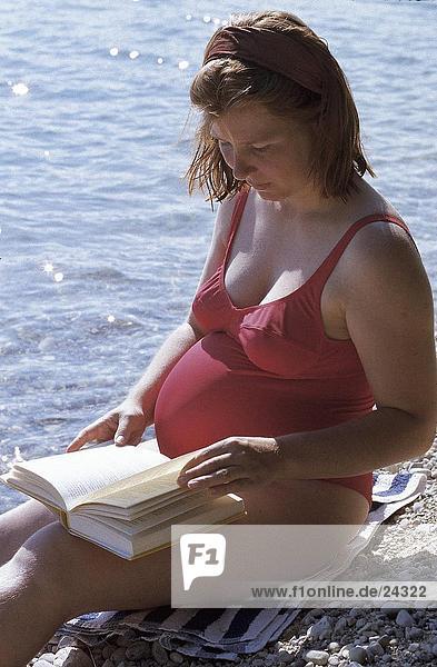 Pregnant woman reading a book at a lakeside
