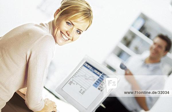 Portrait einer jungen Frau auf einem Computer mit einem jungen Mann stehen im Hintergrund arbeiten