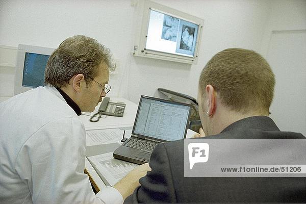 Rear view of two doctors using laptop