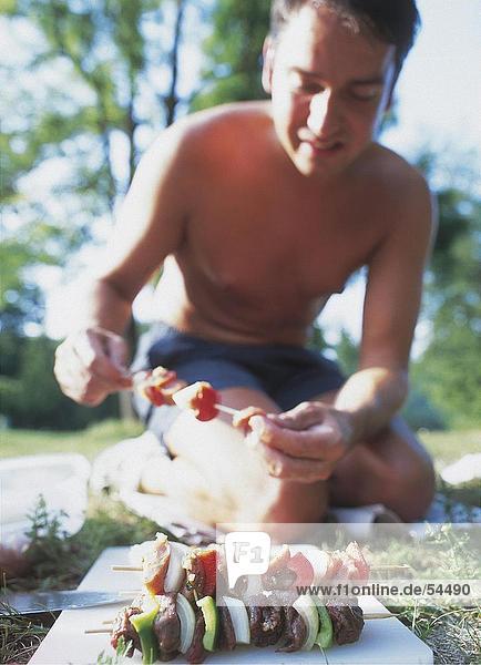 Junger Mann Vorbereitung Kebab während Picknick