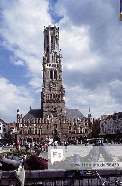 Two men sleeping on wall in front of clock tower  Bruges  Belgium