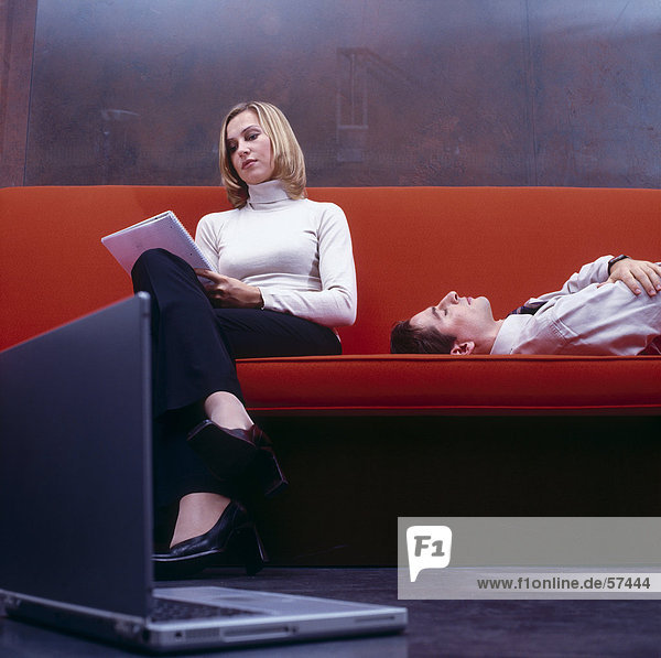 Businesswoman reading documents with businessman sleeping on a couch
