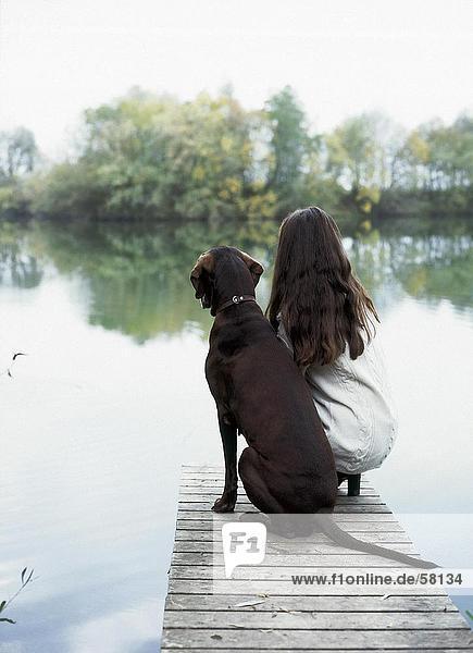 Rückansicht junge Frau sitzt mit Hund am pier