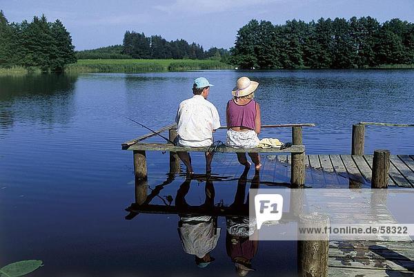 Rückansicht eines Paares sitzen auf eine Pier und Fischerei