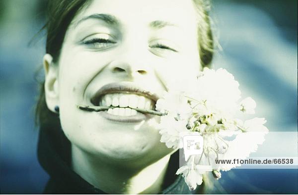 Nahaufnahme der junge Frau hält Blume in den Zähnen und lächelnd