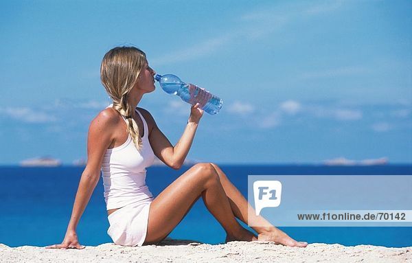 Seitenprofil junge Frau Trinkwassergewinnung aus Flasche am Strand