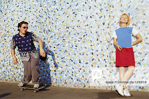 Two young adults near a patterned wall
