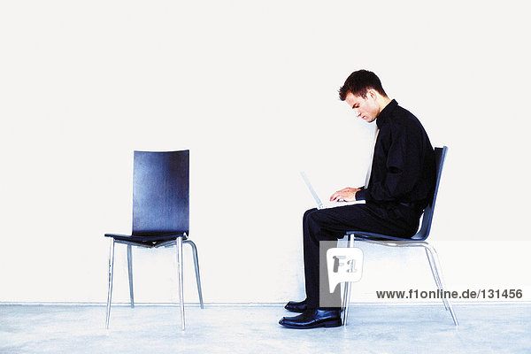 Mann auf Stuhl sitzend mit Notebook