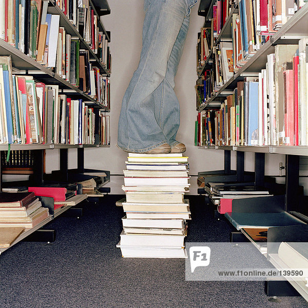Student standing on a pile of books at library