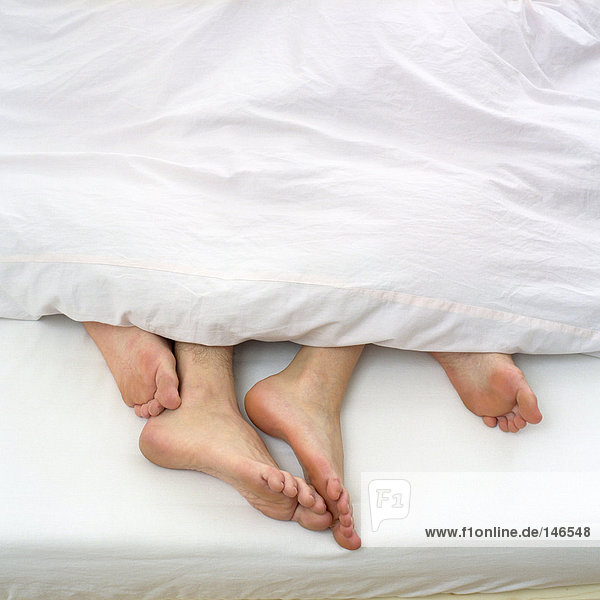 Nackte Füße des Paares im Bett