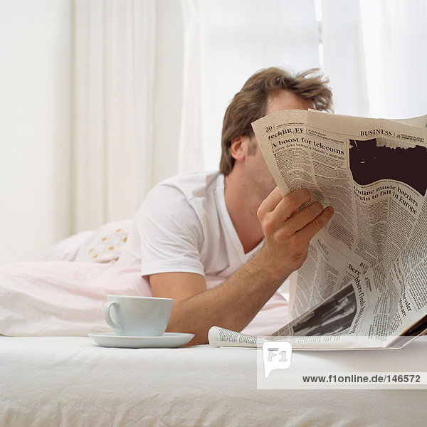 Mann im Bett mit Tee und Papier