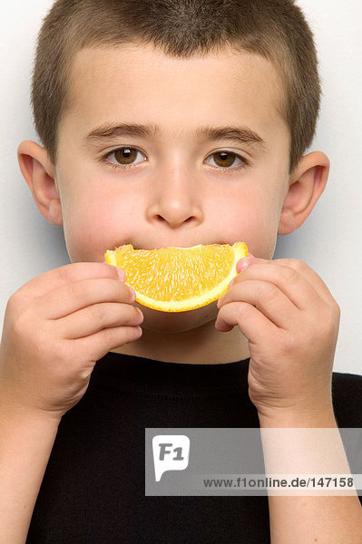 Boy holding orange segment to mouth