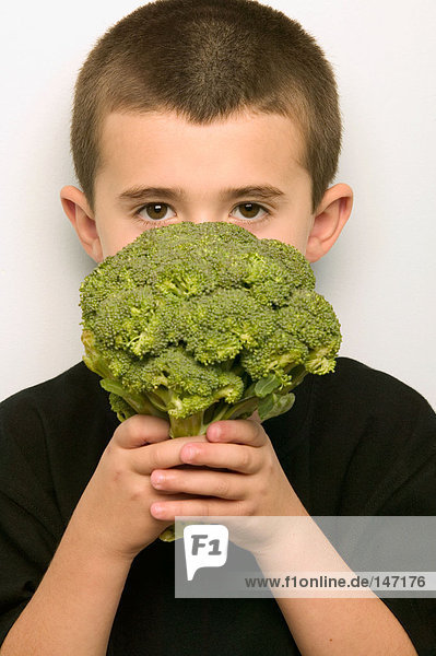 Boy covering face with broccoli