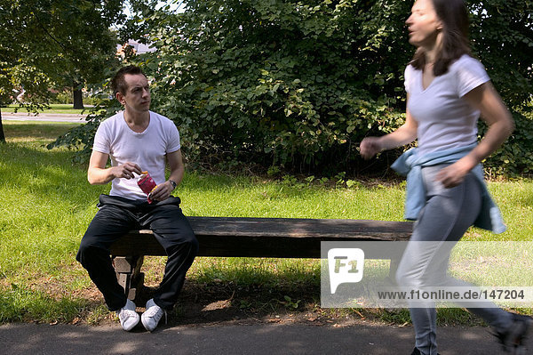 A man sat on a bench and a woman running