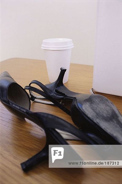 Hochhackige Schuhe und Tasse auf dem Schreibtisch