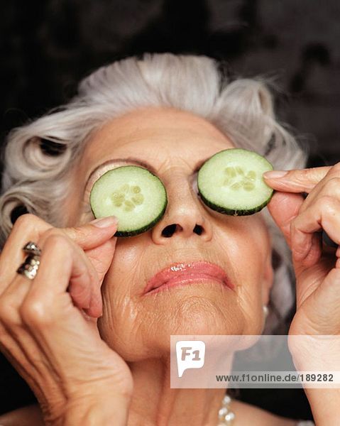 Eine ältere Frau  die Gurken über die Augen hält.