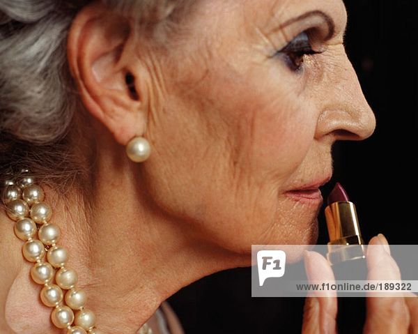 Ältere Frau  die Lippenstift und Mund aufträgt.