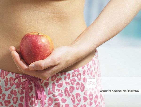 Frau hält einen Apfel an den Bauch