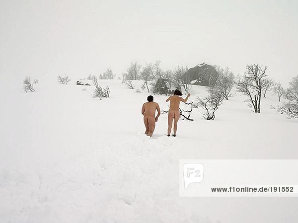 Nacktes Paar  das im Schnee rennt.