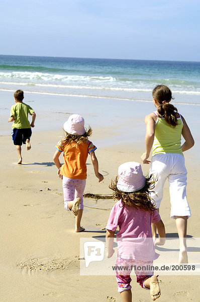 Rückansicht Frau spielen mit ihren drei Kindern am Strand