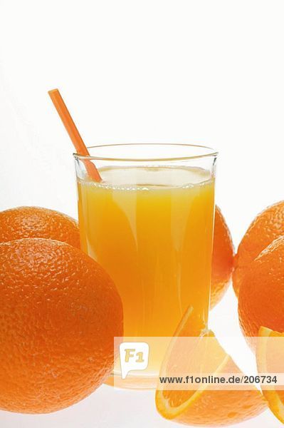 Orangensaft im Glas mit Strohhalm zwischen Orangen
