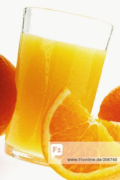Orangensaft im Glas zwischen Orangen
