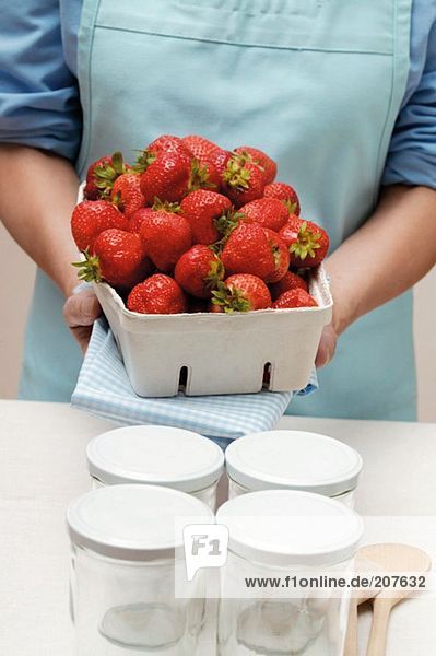 Woman holding punnet of strawberries  jam jars