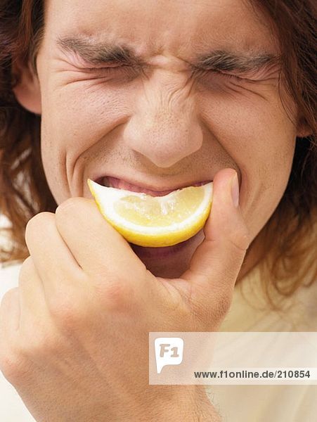 Ein Mann beißt eine Scheibe Zitrone.