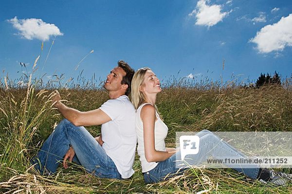 Couple in a field sitting back to back