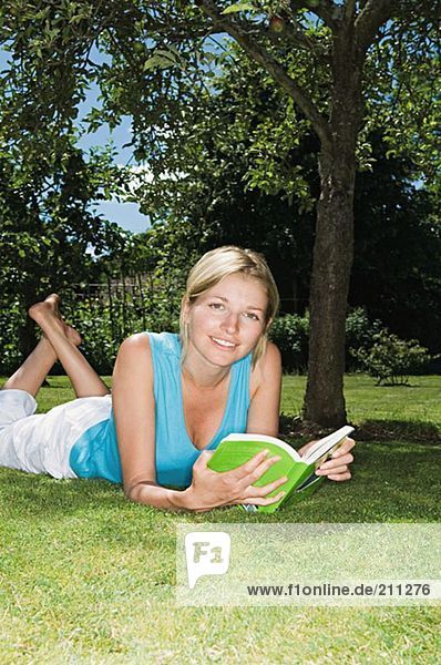 Frau liegt auf dem Gras und liest ein Buch.