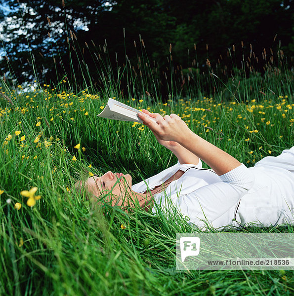 Frau liest Buch auf Gras