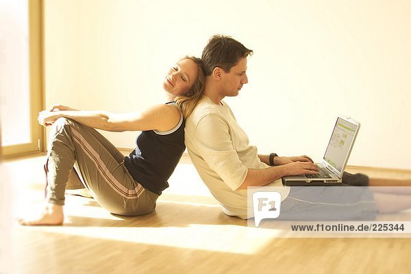 Side profile of young woman leaning against his husband working on laptop