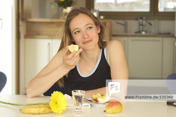 Close-up of young woman eating apple at table