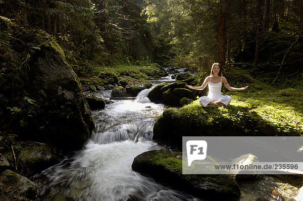 Frau beim Meditieren im Wald am Bach