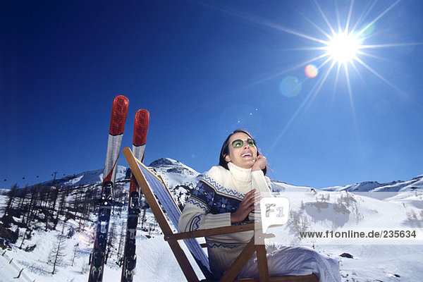 Austria  woman sitting on deckchair in snow alps  smiling  low angle view