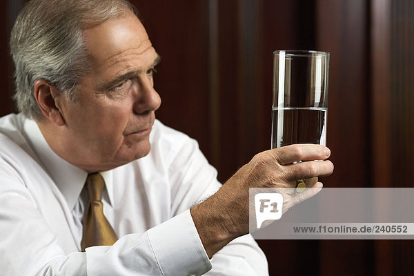 Geschäftsmann schaut nachdenklich auf ein Glas Wasser.