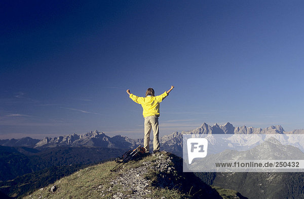 Österreich  Salzburger Land  Mann auf dem Berg mit erhobenen Armen  Rückansicht