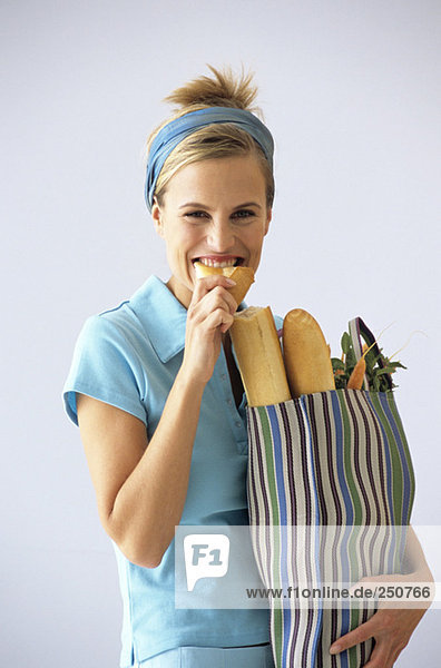 Woman carrying grocery bag,  eating baguette