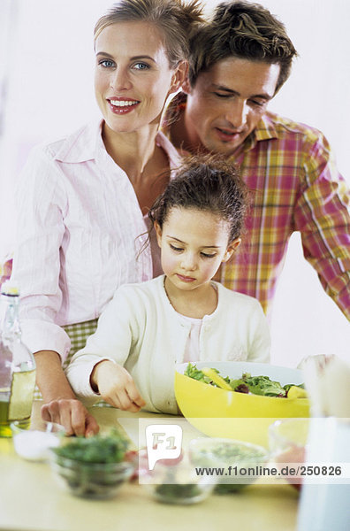 Eltern beobachten Tochter (6-7) beim Zubereiten von Salat