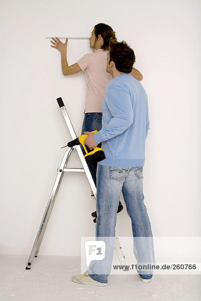 Young couple  man holding electric drill  woman measuring wall with scale