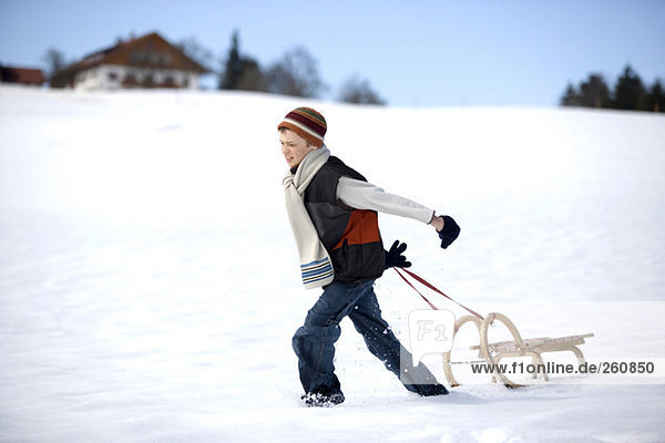 Austria  boy (12-13) pulling sledge in snow  side view