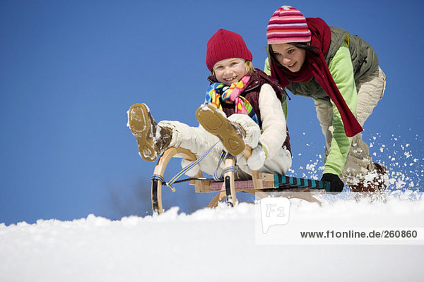 Austria  teenage girl (16-17) pushing girl (6-7) on sledge  smiling  low angle view