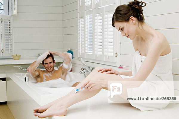 Man having a bath and woman shaving her legs
