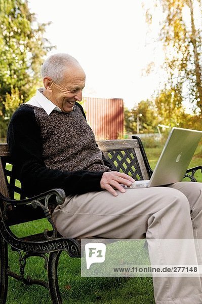 An old man with a laptop in a park.