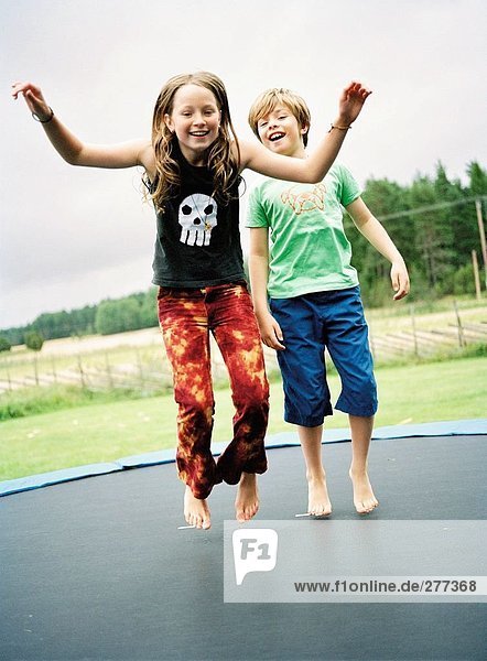 Ein Mädchen und ein Junge auf einem Trampolin Springen.