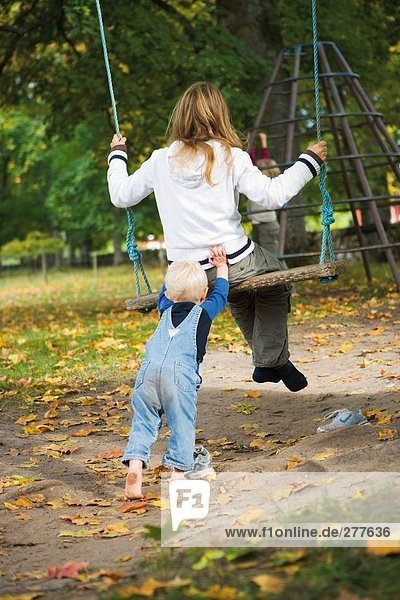 A small girl pushing her sister on a swing.